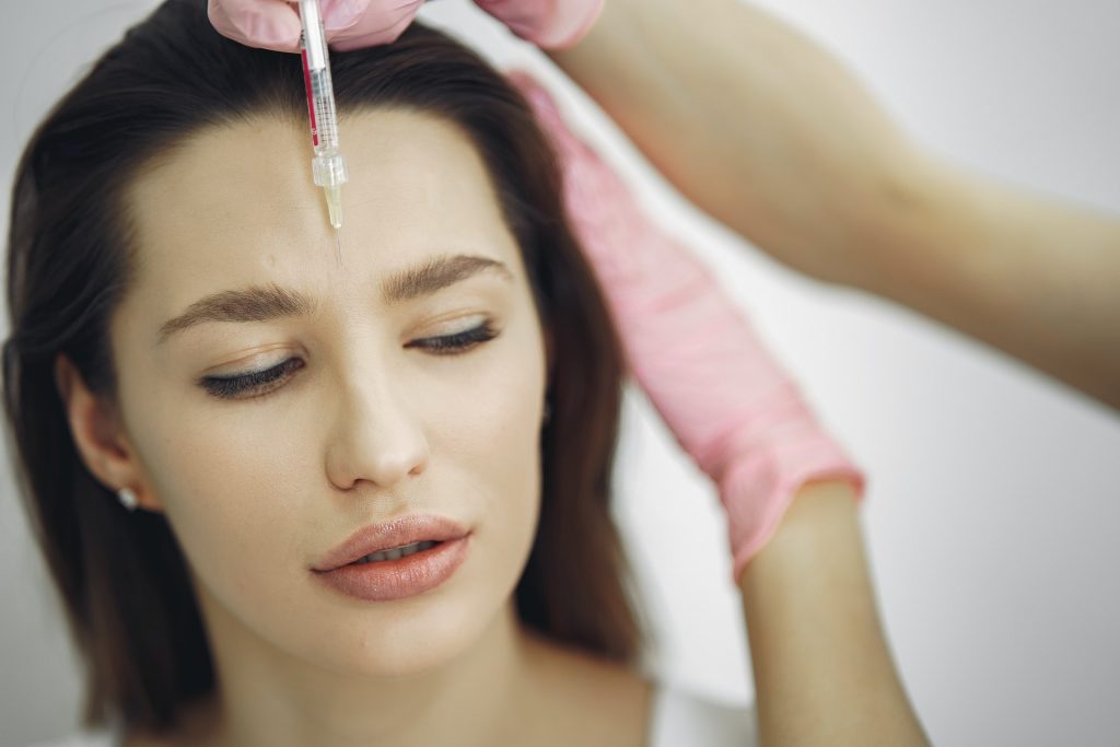 Gloved hands giving a small cosmetic injection near the forehead