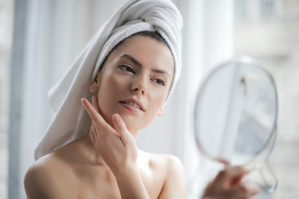 Woman in a towel wrap touching her face while looking in a hand mirror